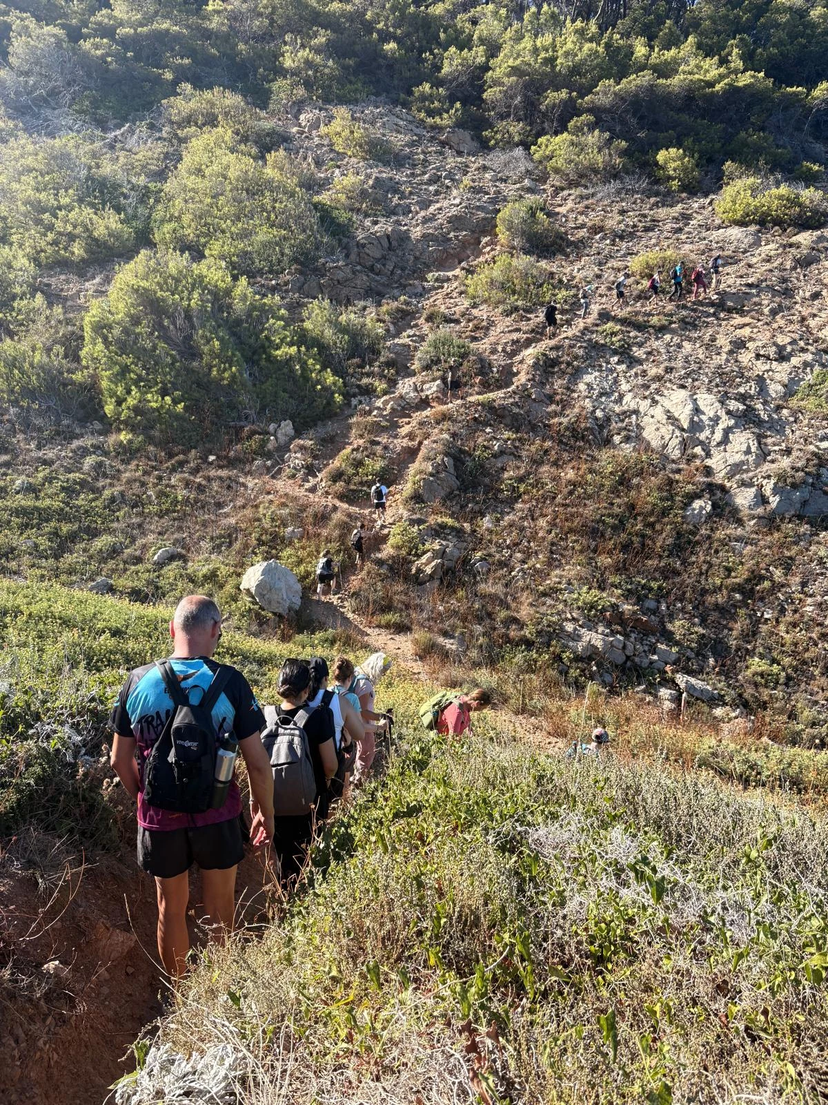 A group following a winding trail through a rocky, green hillside